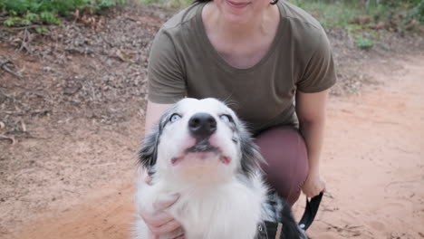 Woman-shows-affection-and-trust-to-her-Australian-Shepherd-dog,-she-holds-him-by-his-leash-and-caresses-him