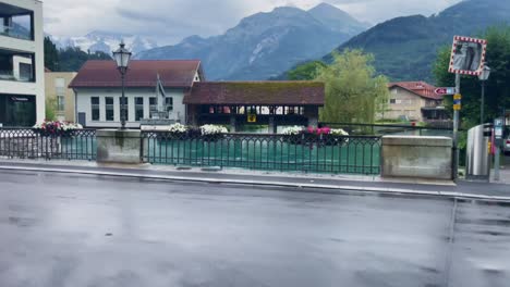 Interlaken-Switzerland-Immersive-Travel-Tourism-Mountainside-Valley-Resort-City,-Europe,-Walking,-4K-|-Looking-Around,-Shaky,-Water,-River,-Lake,-Restaurant,-Parked-Car,-Biker-Moving,-Bridge,-Corner