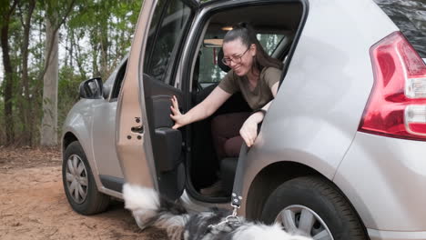 Cheerful-australian-shepherd-and-his-owner,-a-young-woman,-get-out-of-a-parked-gray-car,-ready-for-a-walk-in-the-woods