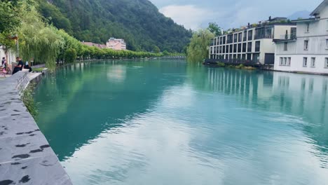 Interlaken-Switzerland-Immersive-Travel-Tourism-Mountainside-Valley-Resort-City,-Europe,-Walking,-Rainy-Day,-4K-|-Looking-Around,-Shaky,-Water,-River,-Lake,-Restaurant,-Tourists,-Wave,-Paragliding