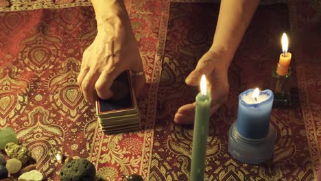 Close-up-of-a-real-tarot-reader's-hands-predicting-the-future-with-tarot-cards-on-a-mystical-table-with-candles-and-gems