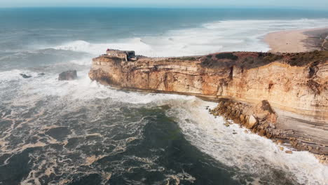 Aerial-view-of-rocky-oecan-with-crashing-waves-in-Nazare,-Portugal