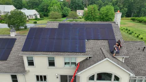 Young-male-solar-employees-installing-panels-on-residential-shingle-roof-with-no-harnesses-or-OSHA-safety-equipment