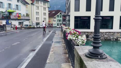 Interlaken-Switzerland-Immersive-Travel-Tourism-Mountainside-Valley-Resort-City,-Europe,-Walking,-Rainy-Day,-4K-|-Looking-Around,-Shaky,-Water,-River,-Lake,-Restaurant,-Flowers,-Bridge,-Family,-Biker