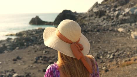 Back-view,-tourist-in-cute-sun-hat-watching-calm-rocky-seaside,-slowmo