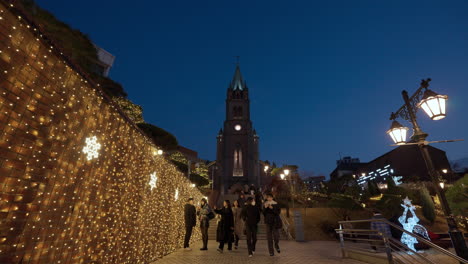 Myeongdong-Kathedrale---Nachtansicht-Von-Menschen,-Die-Stufen-Auf-Und-Ab-Gehen-Und-Fotos-An-Der-Mit-Weihnachtsgirlanden-Geschmückten-Wand-Machen