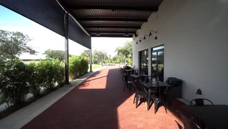 Wide-angle-push-in-below-shade-awning-covering-outside-seating-of-metal-cafe-table-and-seats