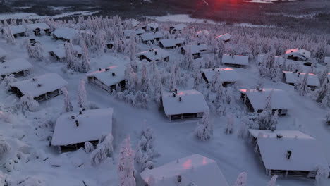 Aerial-overview-of-mountain-lodges-on-top-of-a-snowy-fjell,-sunrise-in-Lapland