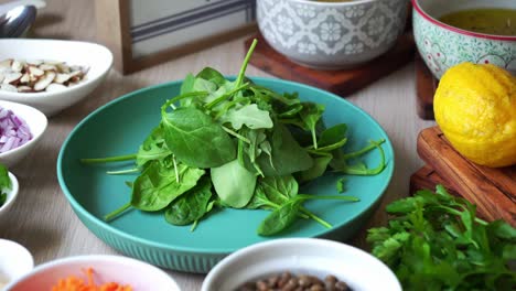 Adding-salad-spinach-leaves-to-plate-with-ingredients-and-salad-dressing-in-the-background