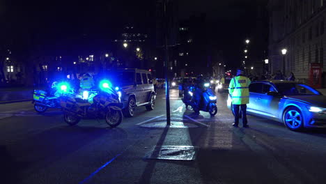 Stadtpolizisten-Stehen-In-Der-Nähe-Von-Zwei-Polizeimotorrädern-Mit-Blaulicht-An-Einer-Straßenkreuzung-Auf-Dem-Parlamentsplatz-Und-Weisen-Nachts-Autos-Und-Motorräder-Weg