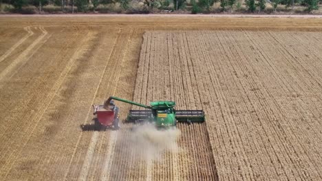 Aerial-view-behind-a-wheat-harvester-working-and-also-unloading-to-a-bin-behind-a-tractor