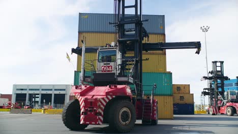 Forklift-truck-preparing-to-lift-heavy-shipping-container-stacked-in-Port-of-Montreal-logistics-dockyard