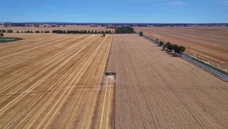 Aerial-moving-along-behind-a-working-wheat-harvester-and-showing-paddocks-and-hills-beyond