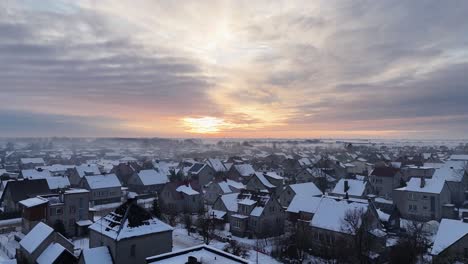 Drone-trucking-pan-aerial-overview-of-snow-covered-roofs-and-subdivision-suburb-with-epic-sunset-and-grey-clouds