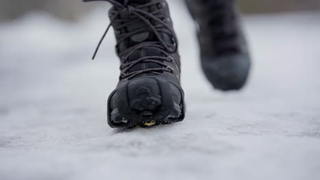 Feet-walking-towards-camera-with-ice-spikes-on-shoes,-handheld-closeup-slow-motion