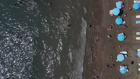 Aerial-view-still-image-of-people-sunbathing-on-the-beach-and-swimming-in-the-sea,-sunbeds-and-umbrellas-on-the-beach