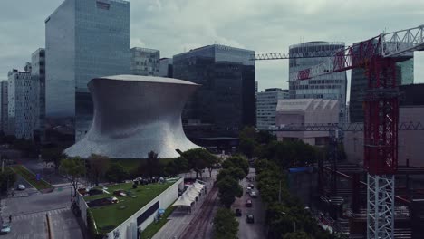 Ascending-drone-shot-of-Soumaya-Museum-and-surroundings,-a-crane-in-a-construction-is-on-the-right,-the-day-is-cloudy