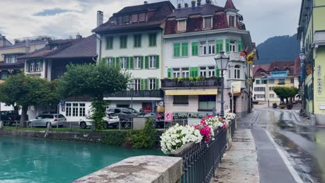 Interlaken-Switzerland-Immersive-Travel-Tourism-Mountainside-Valley-Resort-City,-Europe,-Walking,-Rainy-Day,-4K-|-Looking-Around,-Shaky,-Water,-River,-Lake,-Restaurant,-Out-of-Focus,-Wind,-Flag,-Road