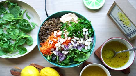 Creating-a-salad-adding-lentils-hummus-to-plate-with-spinach-and-carrots-slices-cilantro-onions-sliced-almonds-dressing-lemons