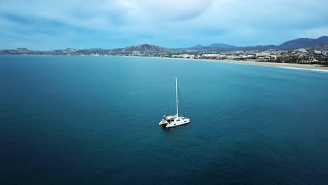 Orbital-drone-shot-with-sailboat-approach-on-the-coast-of-the-Pacific-Ocean-in-Los-Cabos-Mexico
