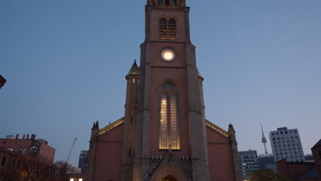 Myeongdong-Cathedral-At-Sunset-with-crowded-people-walking-in-Seoul-city---real-time-tilt-down