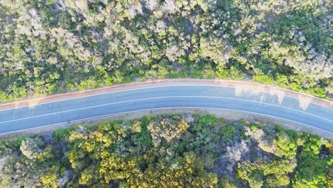 Top-down-drone-shot-of-road-with-car-passing-by-at-sunset