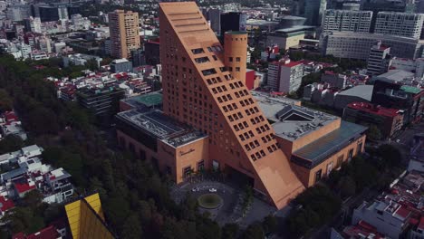 Track-out-drone-shot-of-El-Palacio-de-Hierro-triangular-shape-store-in-Polanco,-Mexico-City-in-a-cloudy-Sunday