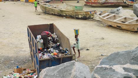 Man-looks-through-garbage-in-dumpster-by-fishing-harbor-in-Ghana,-wide