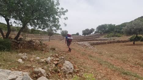 A-solo-male-hiker-walking-through-empty-fields-on-a-little-incline-in-Turkish-Lycian-Way-during-a-hot-summer