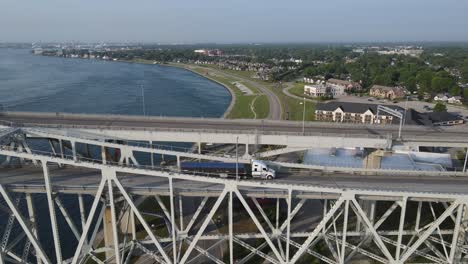 Metal-arch-bridge-in-Port-Huron-with-city-panorama-behind,-aerial-view