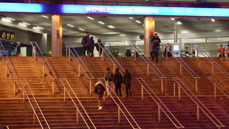 People-in-winter-clothing-walk-up-the-steps-leading-to-the-main-entrance-of-Wembley-Park-Underground-train-station-at-dusk