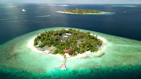 Tropisches-Inselparadies-–-Malahini-Kuda-Bandos,-Malediven:-Luftdrohne-Dreht-Sich-Gegen-Den-Uhrzeigersinn-Von-Oben,-Bandos-Hintergrund-Vom-Steg-Aus
