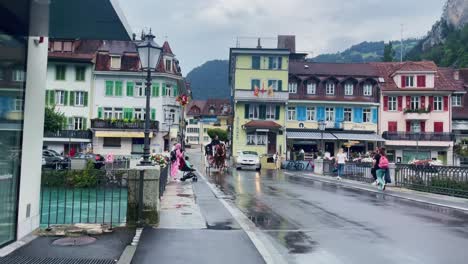 Interlaken-Switzerland-Immersive-Travel-Tourism-Mountainside-Valley-Resort-City,-Europe,-Walking,-Rainy-Day,-4K-|-Looking-Around,-Shaky,-Water,-River,-Lake,-Restaurant,-Woman,-Car,-Horse,-Carriage