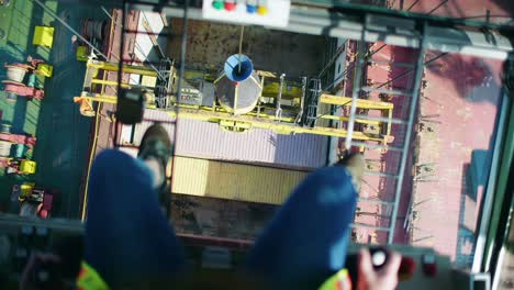 Looking-down-between-industrial-harbour-crane-operator-legs-loading-shipping-containers-in-Port-of-Montreal-dockyard