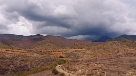 Aerial-view-following-Landcruiser-with-rooftop-tent-driving-towards-stormy-Oaxaca-mountains,-Mexico