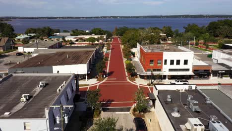 Drone-dolly-above-red-brick-road-and-white-sidewalk-push-in-to-open-blue-lake-in-distance
