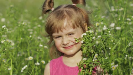 Little-blonde-child-girl-in-pink-dress-stay-on-flower-chamomile-grass-meadow.-Bouquet-of-daisies