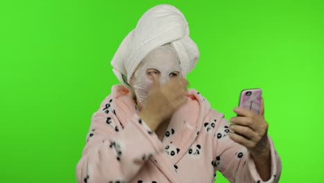 Grandmother-in-bathrobe,-face-mask.-Old-woman-making-selfies-using-mobile-phone