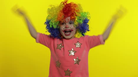 Little-child-girl-clown-in-colorful-wig-making-silly-faces,-shouts,-grabs-her-head,-waves-her-hands