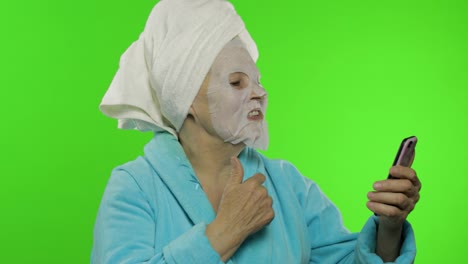 Grandmother-in-bathrobe,-face-mask.-Old-woman-using-mobile-phone-for-video-call