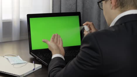 Man-takes-sanitizer-bottle-and-use-near-laptop-with-green-screen.-Distance-work