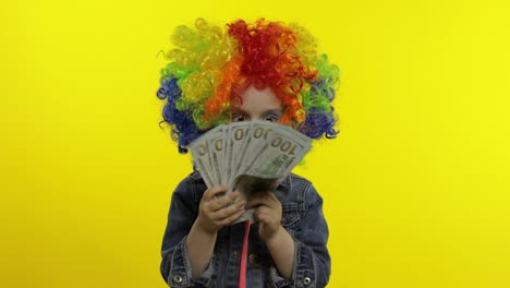 Child-girl-clown-in-colorful-wig-making-silly-faces-with-money-banknotes-dollar-cash.-Halloween