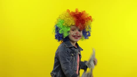Child-girl-clown-in-colorful-wig-dancing-with-money-dollar-cash-banknotes.-Having-fun,-smiling