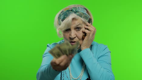 Elderly-caucasian-grandmother-woman-with-money-banknotes-talking-on-mobile-phone