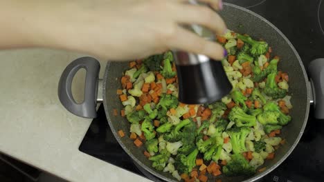 Adding-salt-to-fresh-vegetables-on-frying-pan.-Carrots,-cauliflower,-broccoli