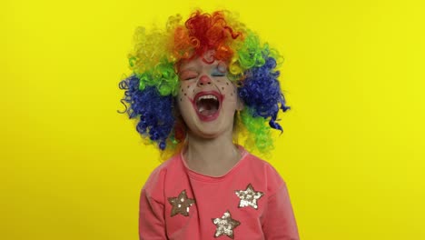 Little-Child-girl-clown-in-rainbow-wig-making-silly-faces.-Having-fun,-smiling.-Thumb-up.-Halloween