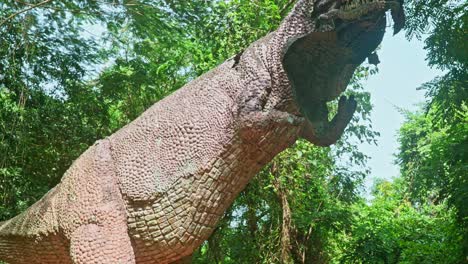 Una-Estatua-De-Un-Dinosaurio,-Una-Estatua-En-Un-Bosque-Arbolado,-Una-Gran-Estatua-De-Un-Dinosaurio,-La-Estatua-Rota