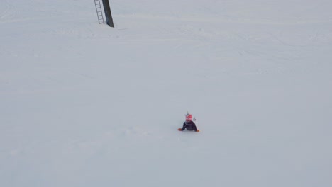 7-year-girl-with-unicorn-helmet-have-fun-sliding-down-snowy-hill,-high-angle-handheld