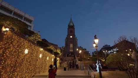 Myeongdong-Kathedrale---Nachtansicht-Von-Menschen,-Die-Stufen-Auf-Und-Ab-Gehen-Und-Fotos-An-Der-Mit-Weihnachtsgirlanden-Geschmückten-Wand-Machen