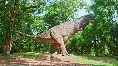 Una-Gran-Estatua-De-Un-Dinosaurio,-Una-Estatua-En-Un-Bosque-Arbolado,-Una-Estatua-De-Un-Dinosaurio,-La-Estatua-Rota